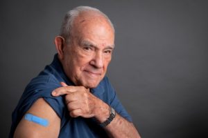 Senior man lifting his shirt sleeve showing his vaccination band-aid on his arm looking at the camera