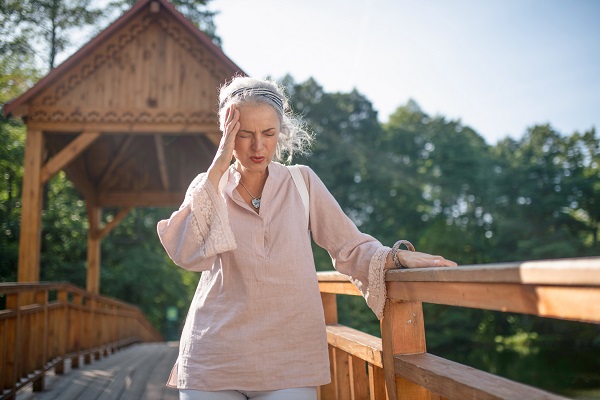 Mature woman holding her head suffering from headache while walking in the park