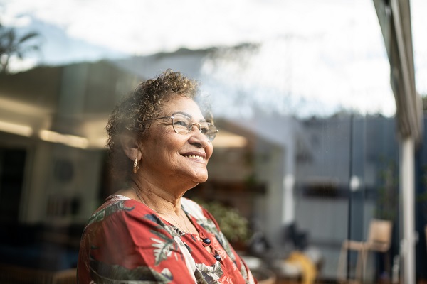 Happy senior woman looking out her window contemplating at home